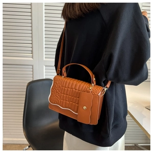 Close-up of brown crocodile pattern bag with white wavy trim and small coin purse charm