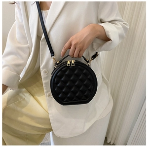 Chic black quilted crossbody bag with gold zippers worn by a model in a white blazer