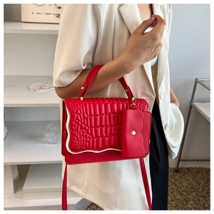 Detail view of red crocodile pattern handbag with white wavy stitching and mini pouch