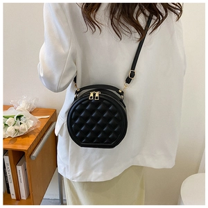Model wearing a black quilted round shoulder bag with gold zipper and adjustable strap