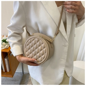 Detail of beige quilted rhombic crossbody bag with golden hardware on a white suit