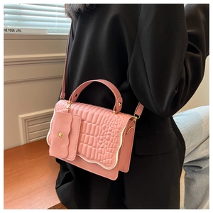 Detail of pink croc-embossed handbag showing gold clasp and wavy pocket on the side