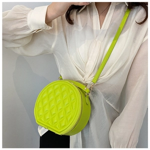 Detail of neon green quilted round crossbody bag with gold hardware on white shirt