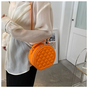 Detail view of round quilted crossbody bag in vibrant orange with adjustable shoulder strap
