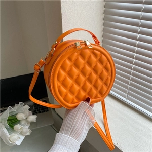 Detailed view of an orange round quilted crossbody bag with gold hardware in a home setting