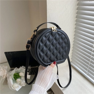Close-up of black quilted leather round crossbody bag with gold dual zipper details