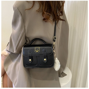Detail of minimalist black PU shoulder bag featuring golden bear logo and plush charm