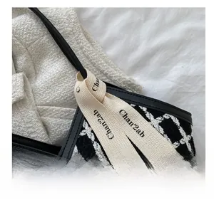 Detail of checkered woven tote with black leather trim and decorative fabric ribbon
