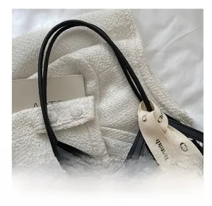 Detail of checkered woven tote bag with slim leather handles and decorative ribbon