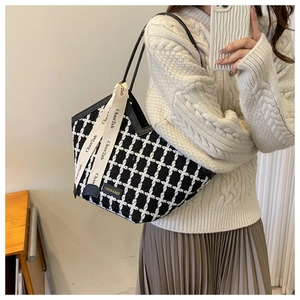 Close-up of black and white checkered tote bag featuring decorative branded ribbons and strap