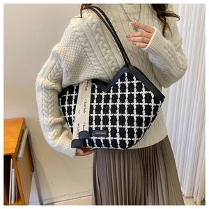 Detail of checkered tweed tote bag with logo ribbon worn on shoulder with cream sweater