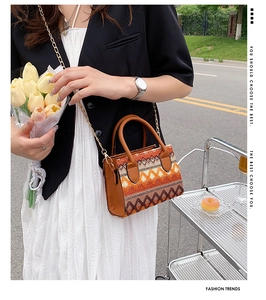 Detail of colorful woven handbag featuring a leather handle and a golden metal chain strap