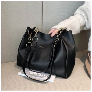 Dettaglio borsa tote nera in pelle con catena dorata ed etichetta Fashion su tessuto grigio