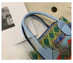 Detail of colorful woven straw handbag featuring light blue leather handle and wave pattern