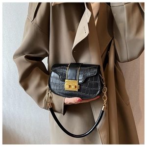 Détail du sac selle noir motif crocodile avec boucle dorée sur un manteau kaki