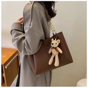 Detail of dark brown tote bag featuring golden metal chain straps and cute bear pendant