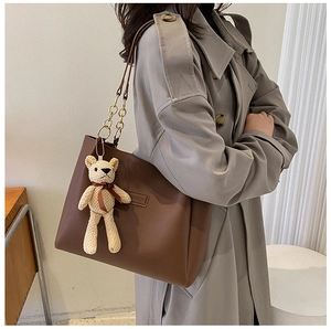 Detail of dark brown tote bag with metal chain strap and cute cream bear charm