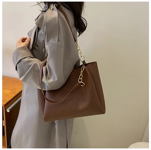 Detail of brown matte leather tote bag featuring embossed logo and gold chain shoulder strap