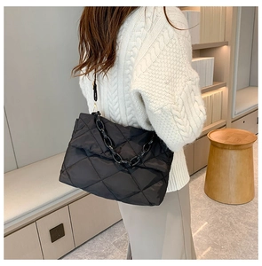 Détail d'un sac bandoulière noir matelassé avec chaîne porté par un mannequin en style décontracté
