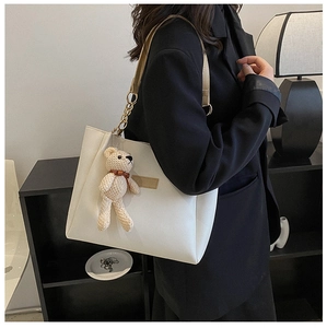 Detail shot of cream PU leather tote bag featuring a cute knitted teddy bear pendant charm