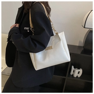 Close-up of white leather tote bag with gold chain strap and metal fashion tag