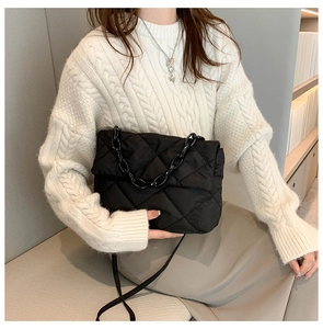 Détail d'un sac bandoulière matelassé noir avec chaîne en résine porté par un mannequin