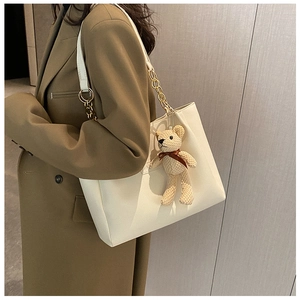 Detail of off-white PU leather tote with gold chain strap and brown knit bear charm