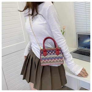 Close-up of ethnic woven handbag with red leather handles and gold chain strap details