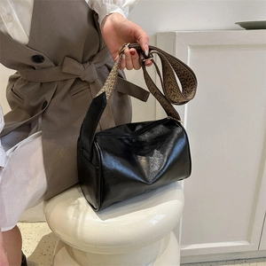 Minimalist black cylinder shoulder bag with glossy finish and patterned wide strap