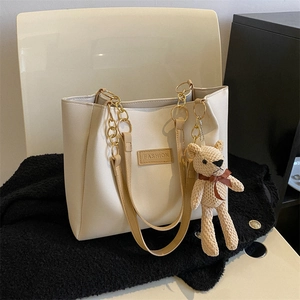 Cream PU leather tote bag with chain decor and a cute knitted bear pendant at a 45-degree angle
