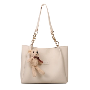 Minimalist beige tote bag with gold chain straps and knit bear charm on white background