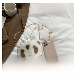 Compact cow print plush bucket bag with gold chain strap and drawstring closure