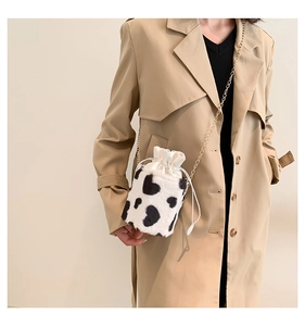 Close-up of plush cow print bucket bag with gold chain strap on a trench coat