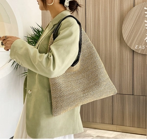 Detail of a large woven straw beach tote bag with black leather handles on a model