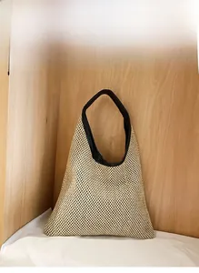 Detail of khaki straw tote bag with black leather trim and handles against wooden wall