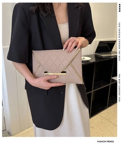 Pochette enveloppe matelassée beige avec bordure dorée tenue par un mannequin en costume
