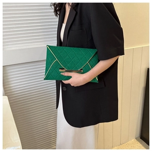 Détail d'une pochette enveloppe verte matelassée avec bordure dorée tenue par un mannequin