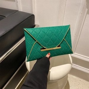 Gros plan d'une pochette enveloppe vert émeraude avec tissu matelassé et bordure dorée