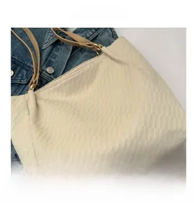 Detail showing cream checkered tote bag texture with khaki leather handles and metal hardware