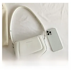 Detailed top view of white minimalist leather shoulder bag next to a smartphone