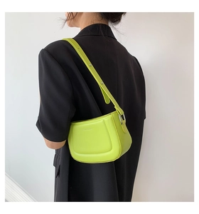 Model wearing a grass green crescent-shaped mini shoulder bag with a black blazer