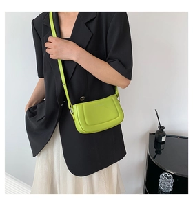 Detail of fruit green leather crossbody bag worn over a black blazer and white skirt