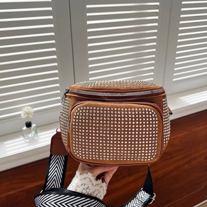 Detail of a brown suede rhinestone bucket bag featuring a woven herringbone shoulder strap