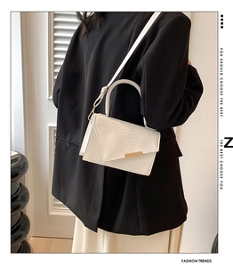 Detail of white faux leather crossbody bag with snake texture and gold buckle on model