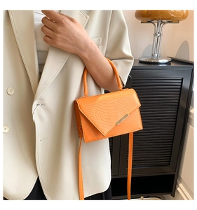 Detail of bright orange crocodile embossed handbag paired with a beige suit