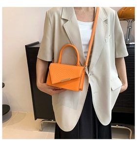 Detailed view of an orange crocodile pattern crossbody bag with a golden metal bar closure