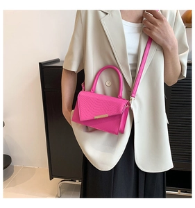 Detail of rose pink crocodile pattern handbag with gold hardware worn by a model