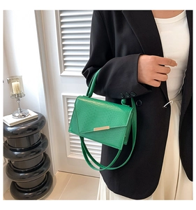 Detail of green crocodile texture handbag with gold buckle styled on a model outfit
