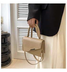 Detail of beige faux crocodile leather handbag with asymmetric cut and gold metal trim