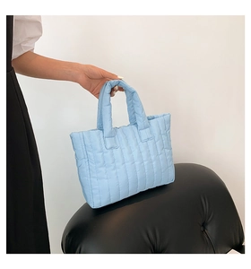 Detail of light blue quilted nylon tote bag with vertical stitching on a black leather seat